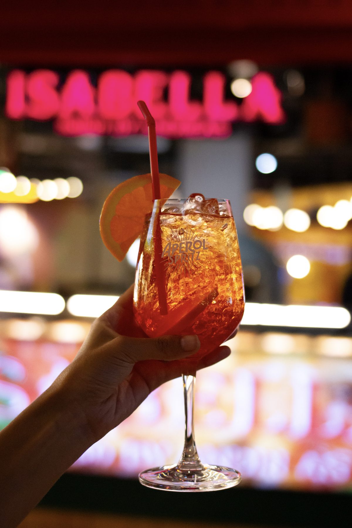 An Aperol Spritz in front of the Isabella neon sign